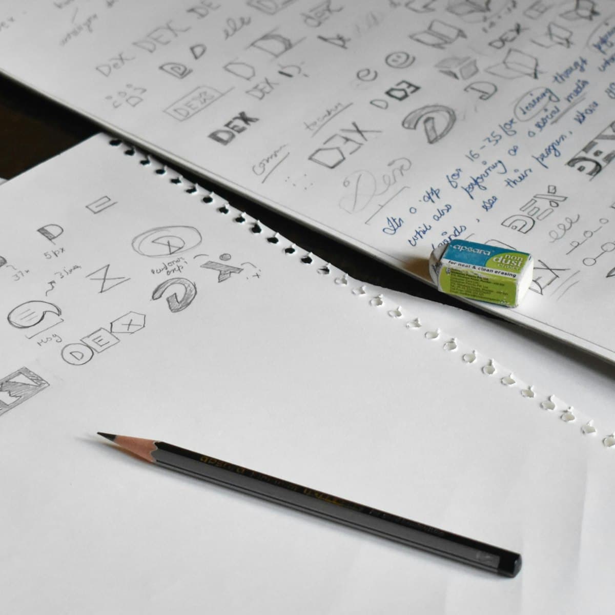 Carnet de croquis rempli de recherches de logo au crayon, avec une gomme et un crayon posés sur la table