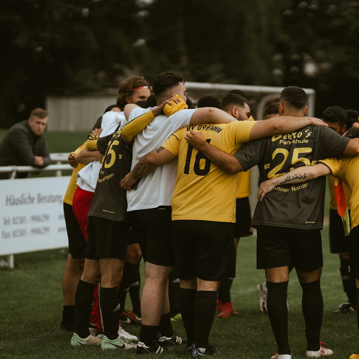 Joueurs d'un club amateur réunis en cercle, maillots floqués du logo d'un partenaire local et panneau sponsor en bord de terrain