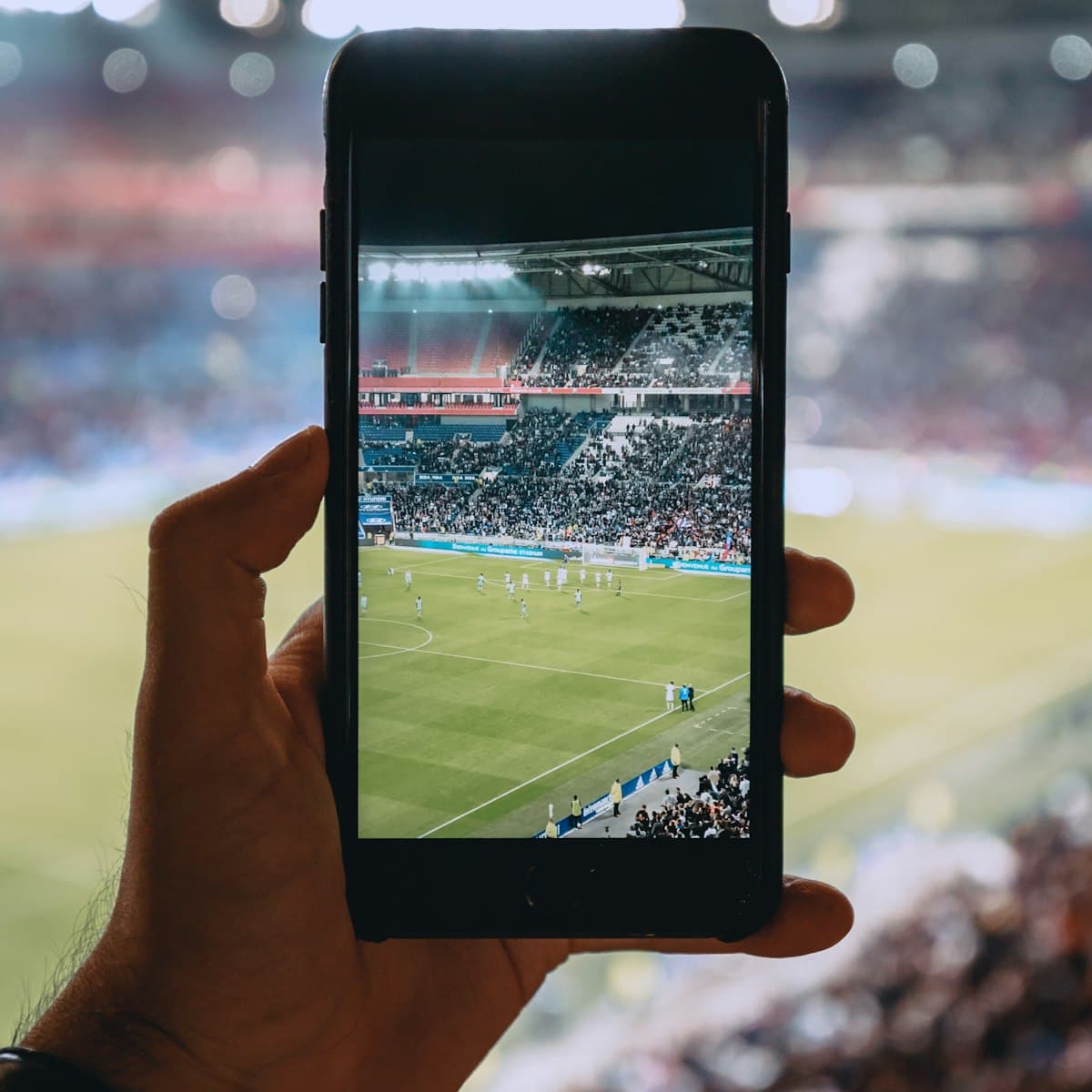Supporter filmant un match de football au smartphone depuis les tribunes d'un stade